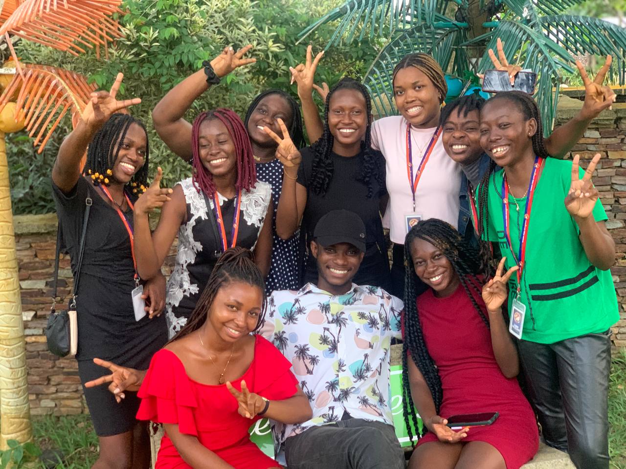 Seven Kings & Priests friends sit closely on outdoor decking, smiling together amid greenery.
